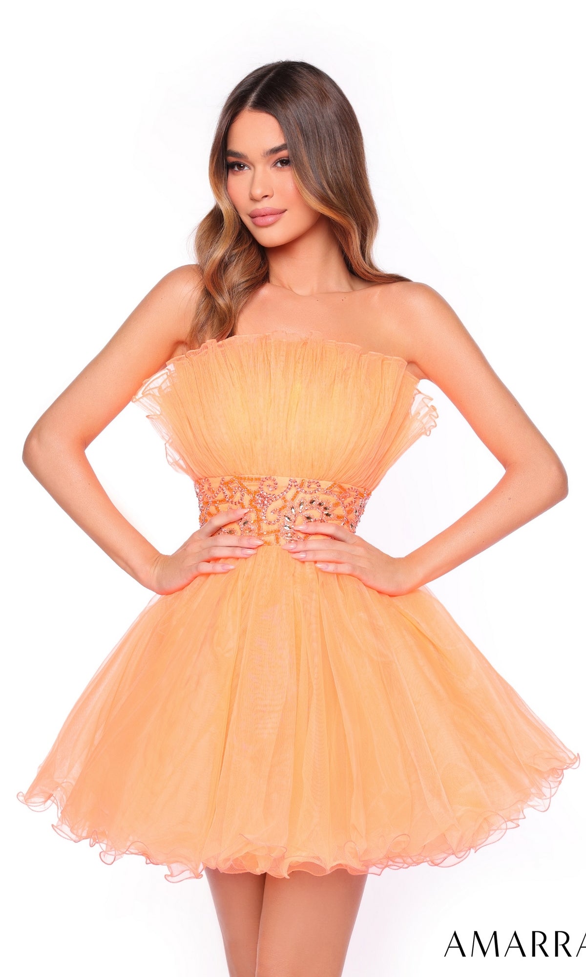 Model in the Amarra Short Homecoming Dress 88038, a strapless, peach mini dress with a beaded waist, stands with hands on hips against a white background.